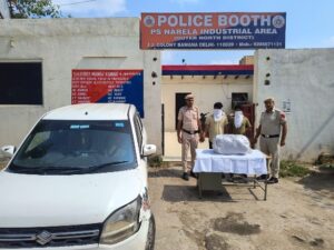 नरेला गांजा मामले में दो और आरोपी पकड़े गए, 14.774 किलो अतिरिक्त बरामदगी दिल्ली पुलिस की तस्वीर में नरेला औद्योगिक क्षेत्र पुलिस बूथ के बाहर पुलिसकर्मी, चेहरा ढके दो व्यक्ति, पैकेट और कार।