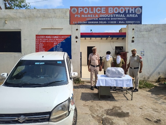 दिल्ली पुलिस की तस्वीर में नरेला औद्योगिक क्षेत्र पुलिस बूथ के बाहर पुलिसकर्मी, चेहरा ढके दो व्यक्ति, पैकेट और कार।