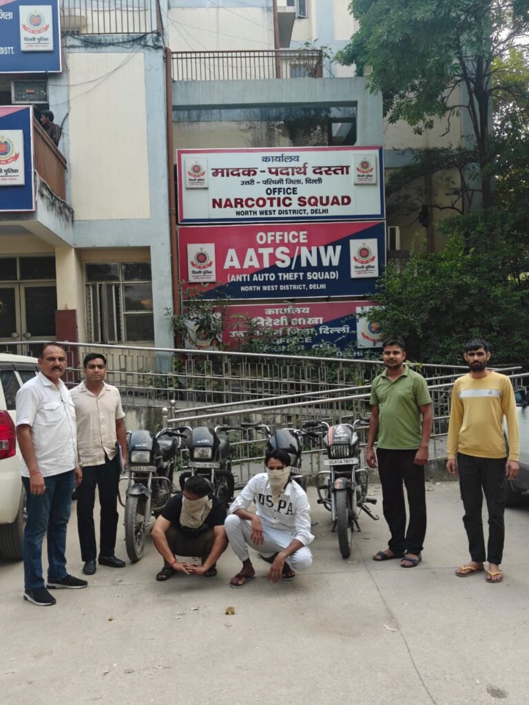 एएटीएस उत्तर-पश्चिम दिल्ली कार्यालय के बाहर चार मोटरसाइकिलें, पास में अधिकारी और चेहरे ढके दो व्यक्ति
