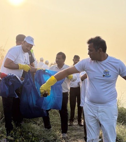 दिल्ली में यमुना सफाई अभियान के दौरान दस्ताने पहनकर थैलों में कचरा इकट्ठा करते प्रतिभागी