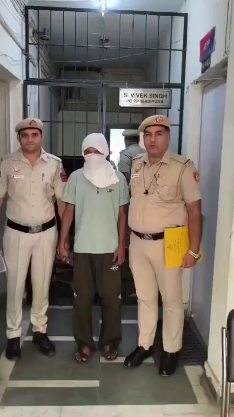 सिधीपुरा पुलिस पोस्ट के बाहर दो पुलिसकर्मियों के बीच खड़ा ढके चेहरे वाला व्यक्ति