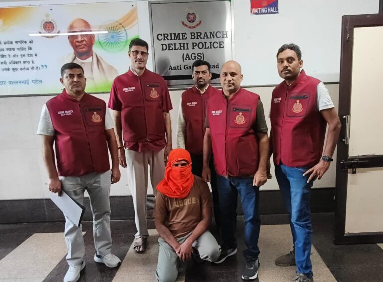 आधिकारिक पुलिस तस्वीर में चेहरा ढके बैठे व्यक्ति के पीछे क्राइम ब्रांच के अधिकारी