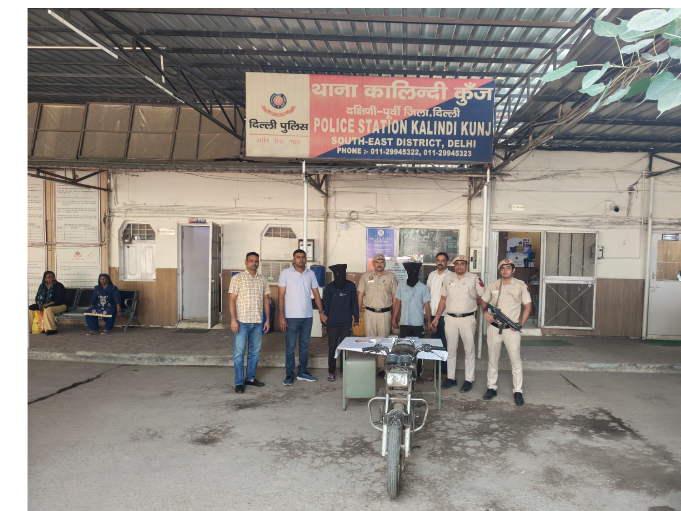 कालिंदी कुंज थाने में पुलिसकर्मियों, चेहरे ढके हुए दो लोगों और मोटरसाइकिल की तस्वीर